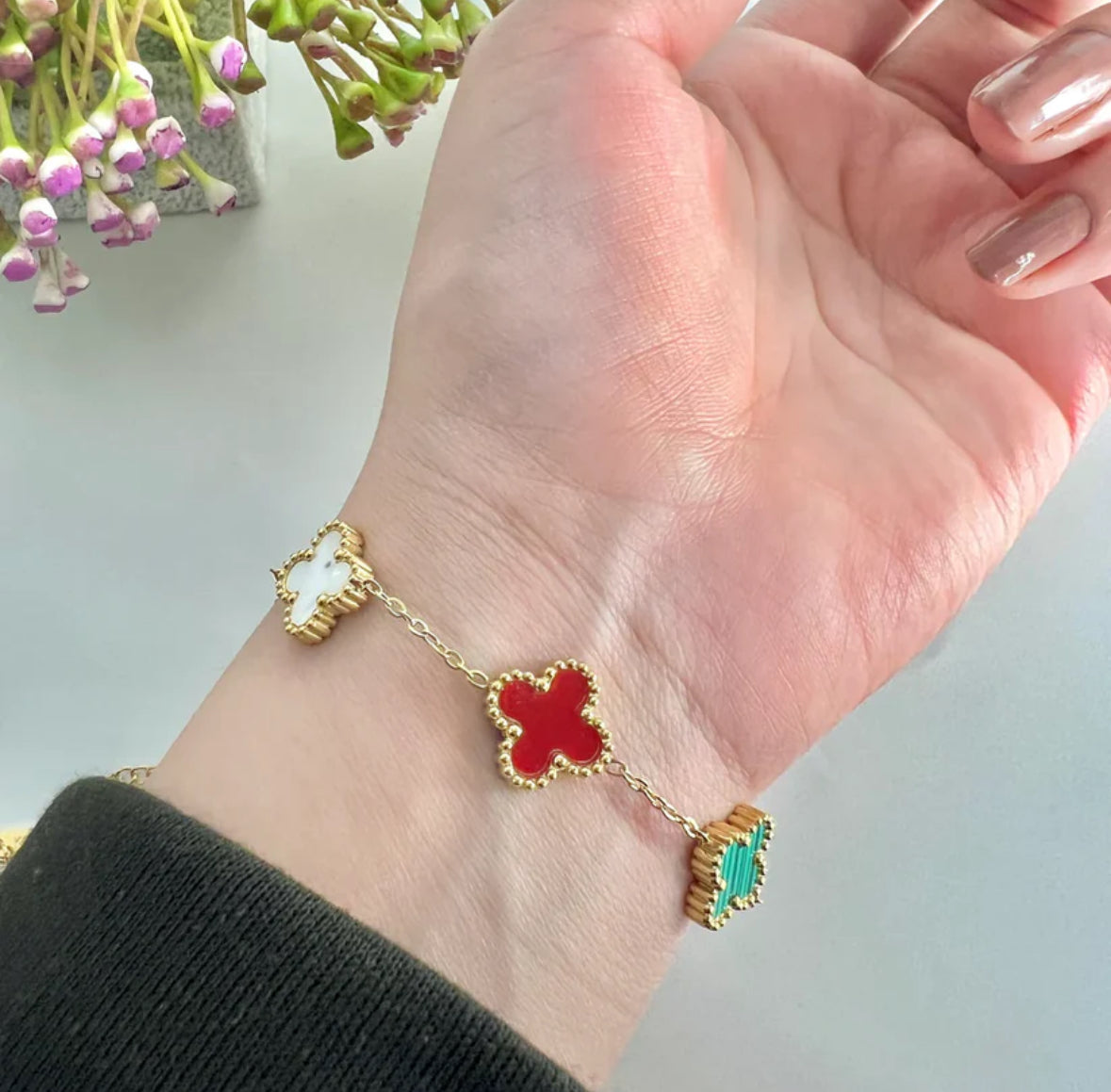 Hand wearing a gold bracelet with red and green flower-shaped